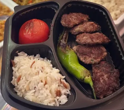 Pilav, domates ve biberle sunulan ızgara köfte